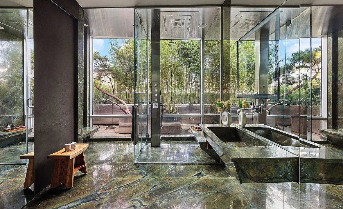 Bathroom with green marble floors and trough sink, a glass shower and a view of the bamboo garden