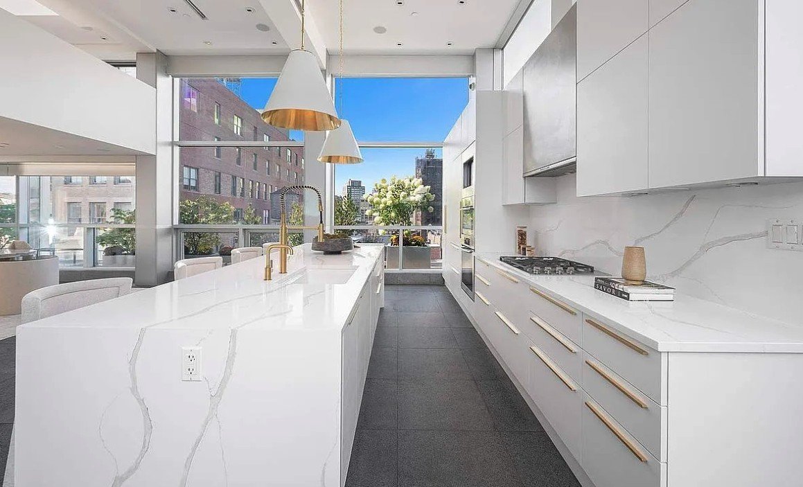 Kitchen with a waterfall marble island, brass fixtures and floor-to-ceiling windows
