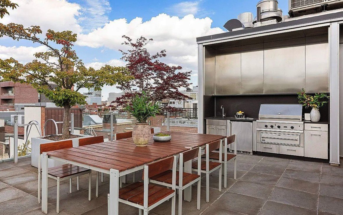 Rooftop dining table beside a stainless-steel outdoor kitchen with grill, sink and refrigerator