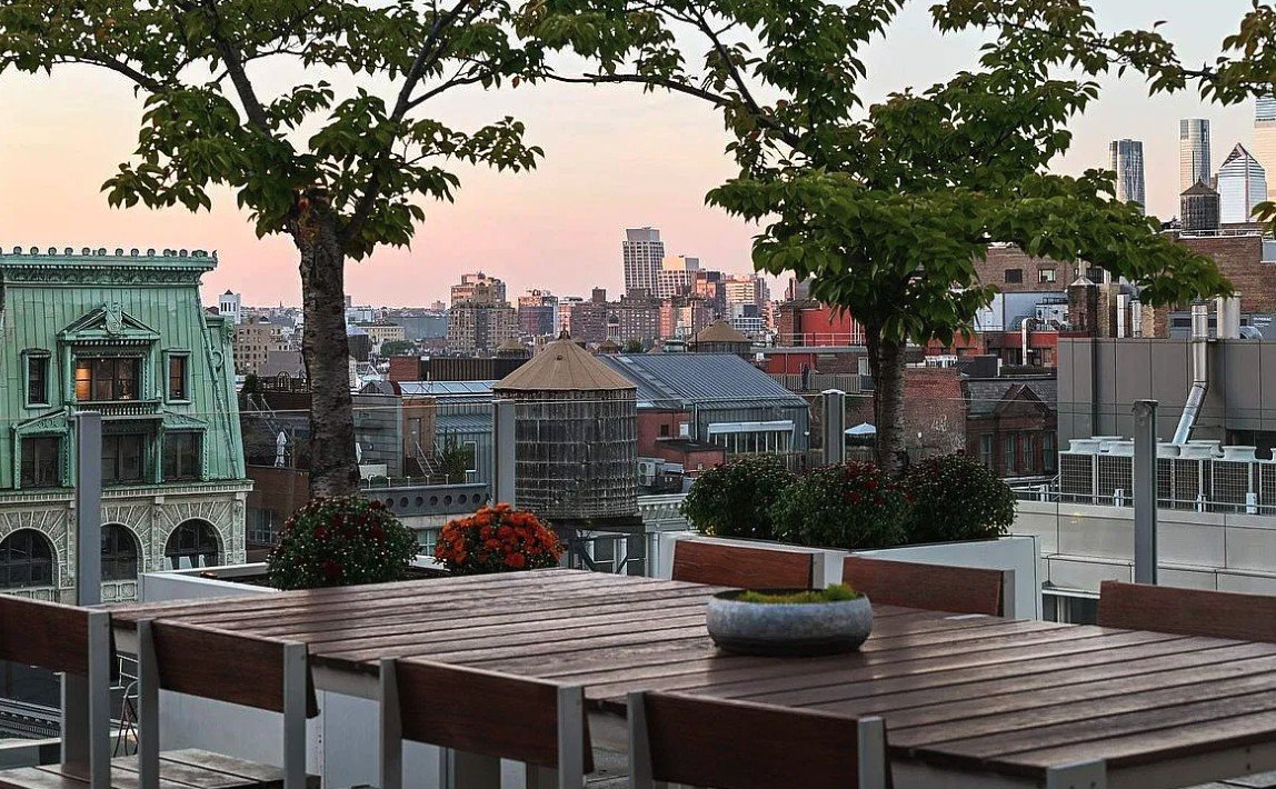 Terrace dining table under trees at sunset, overlooking SoHo rooftops and water towers
